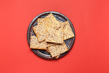 Tasty crackers with seeds in plate on color background