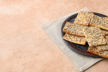 Tasty crackers with seeds in plate on color background