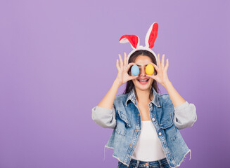 woman smiling wearing rabbit ears and denims holding colorful Easter eggs front eyes