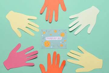 Paper human palms and greeting card for Friendship Day on color background