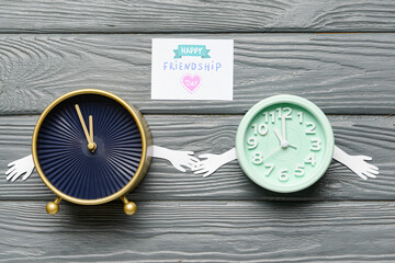 Funny alarm clocks and greeting card for Friendship Day on wooden background