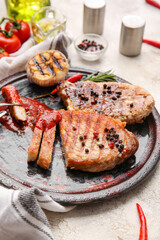 Plate with tasty steaks and spices on light background