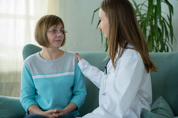 Fototapeta premium Doctor visiting elderly woman at home. Female doctor consoling senior woman during home visit