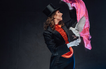 Attactive female sorcerer shows tricks with bird and pink scarf