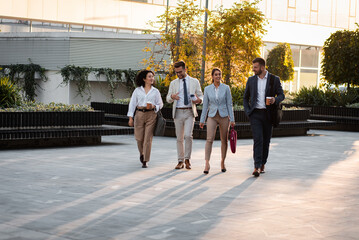 Group of business people walking outside in front of office buildings. - Powered by Adobe