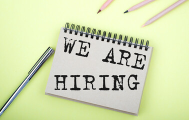 WE ARE HIRING text on the notebook with pen on the yellow background