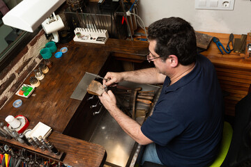 goldsmith sands a silver ring on the workbench.