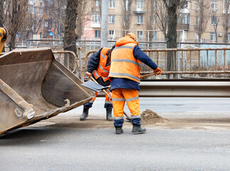 The road workers use shovels to scrape off the sand accumulated between the lanes of the road and load it into the grader bucket.