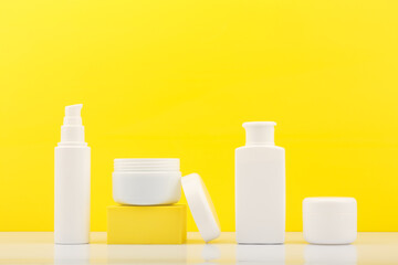 Set of cosmetic bottles with products for skin care against bright yellow background