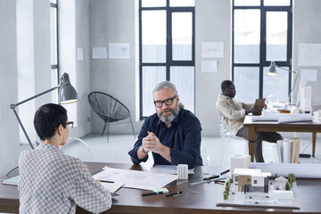 Group of engineers sitting at the table at meeting and working with blueprints at modern office