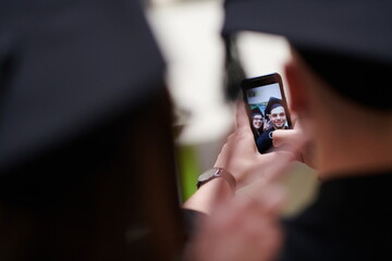 group of happy international students in mortar boards and bachelor gowns with diplomas taking selfie by smartphone