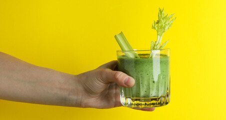 Female hand hold glass of smoothie on yellow background