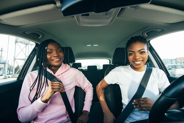 Beautiful young african women is fastening seat belts and smiling while travelling by car