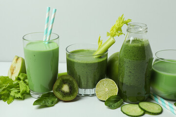 Glasses of green smoothie and ingredients on white table