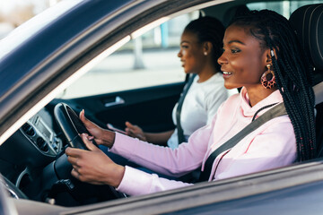 Two african young women on car trip driving the car and making fun.