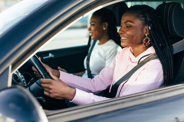 Two african young women sitting in a car and laugh while have road travel