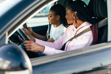 Two african young women driving using navigation on mobile phone on the road trip. Get lost.