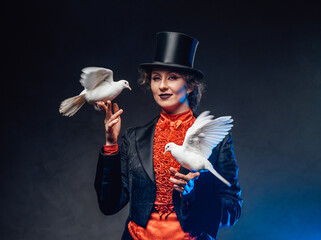 Smiling female magician with two white little doves in dark background