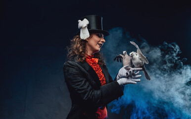 Elegant actress wearing dark clothing with trained doves in smoke