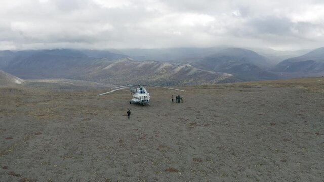 Aerial view of a helicopter and a group of hikers on a mountain top. Clip. Concept of adventure and tourism, people exploring wild natural hilly region.