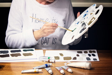 Pretty woman painting with brush and acrylic paints in artistic studio. Pensive female standing at easel with colorful picture.