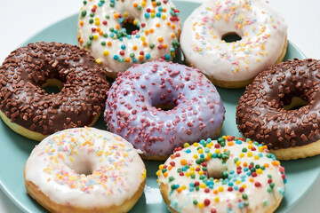 Freshly baked. Various delicious colourful round glazed donuts with sprinkles on the plate