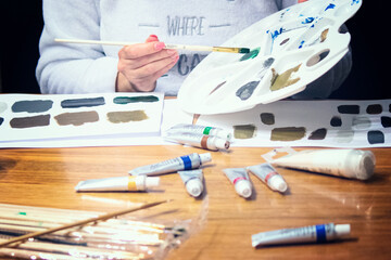 Pretty woman painting with brush and acrylic paints in artistic studio. Pensive female standing at easel with colorful picture.