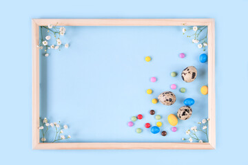 Easter card with Iris flower, quail eggs, colorful candies on blue background.