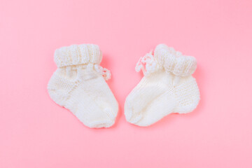 knitted baby booties on pastel pink background.