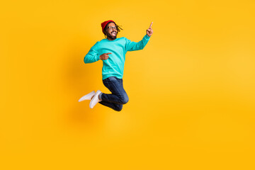 Fototapeta na wymiar Full size profile photo of brunette hooray guy jump point empty space wear cap spectacles pullover jeans sneakers isolated on yellow color background