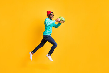 Fototapeta na wymiar Full size profile photo of brunette optimistic guy jump run take present wear cap spectacles pullover jeans isolated on yellow background