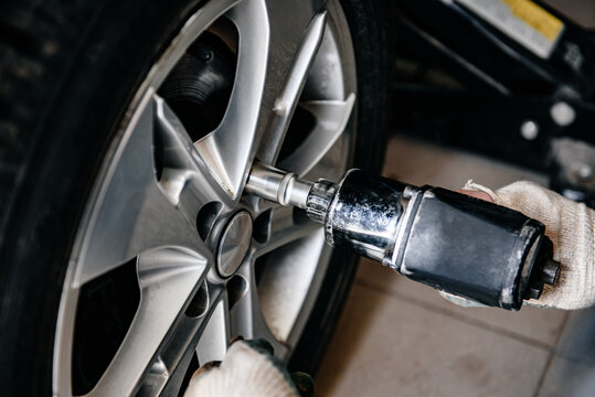 Man doing tire or wheel replacement with pneumatic wrench in garage. Changing car wheel.