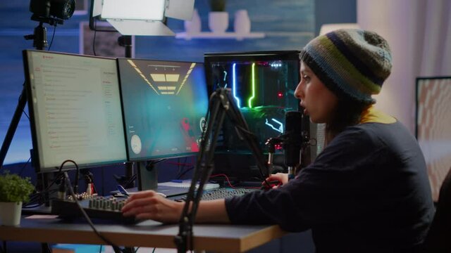 Professional woman streamer playing FPS games talking into microphone via streaming chat during online esports tournament. Gamer making online videogames with new graphics on powerful computer