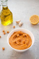 A bowl of delicious hummus with olive oil, garlic and paprika on a grey background.