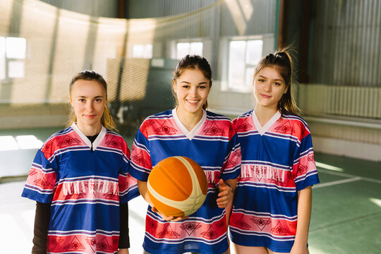 Portrait of high school teen girls with basketball ball court indoors. Members of the female school basketball team standing and smiling , looking at camera
