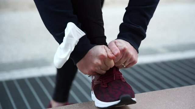 Close up of the hands of a man while tying his shoelaces leaning against a bench before starting his run with the protective face mask on his arm against Coronavirus Covid-19 infections