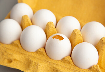 A set of white eggs, one of which is opened in a yellow cardboard box