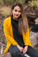 Woman sitting in a tree with a yellow coat in the forest or park in spring. Hat on top of tree.