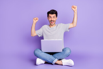 Photo of guy sit floor hold computer raise fists open mouth wear white t-shirt jeans sneakers isolated violet background