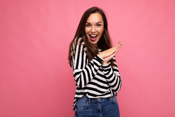 Photo of young positive happy emotional beautiful brunette woman with sincere emotions wearing casual striped pullover isolated on pink background with copy space