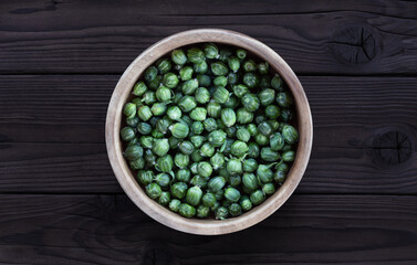 Dandelion buds, capers in wooden bowl on a dark wooden background. Young unblown for pickling....