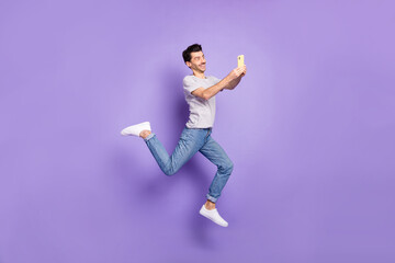 Fototapeta na wymiar Photo of guy jump hold telephone texting wear white t-shirt jeans footwear isolated purple background