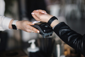Female customer making wireless or contactless payment using smartwatch. Closeup of hands during payment. Store worker accepting payment over nfc technology