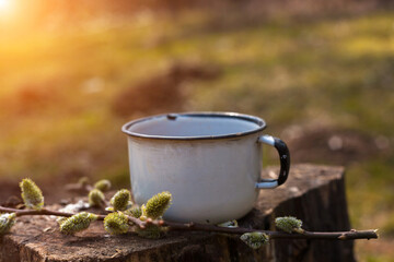 Enamel cup of coffee or tea, on a wooden board in a summer forest outdoors. Place for your text. 