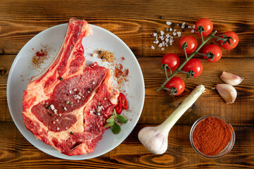 Raw meat with a bone on a white plate.  Cherry tomatoes, garlic, spices. Wooden table. Top view.