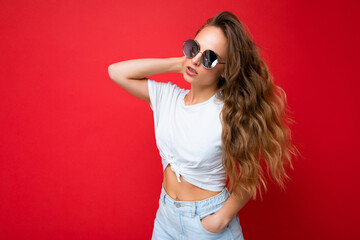 Fototapeta premium Attractive sexy young blonde woman wearing everyday stylish clothes and modern sunglasses isolated on colorful background wall looking to the side