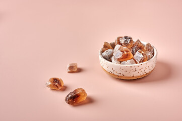 Brown caramelized lump cane sugar cubes in a bowl on pink powdered background, selective focus, copy space