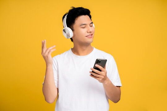 Happy Young Asian Man Wearing Wireless Headphones Listening To His Favorite Music On A Smartphone.