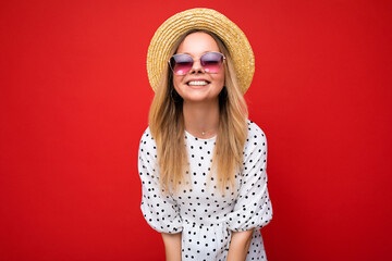 Photo shot of beautiful positive young blonde woman wearing summer casual clothes and stylish sunglasses isolated over colorful background looking at camera