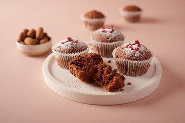 Homemade chocolate cupcakes in baking paper forms and piece of it on light plate on pink powdery background, selective focus, close up